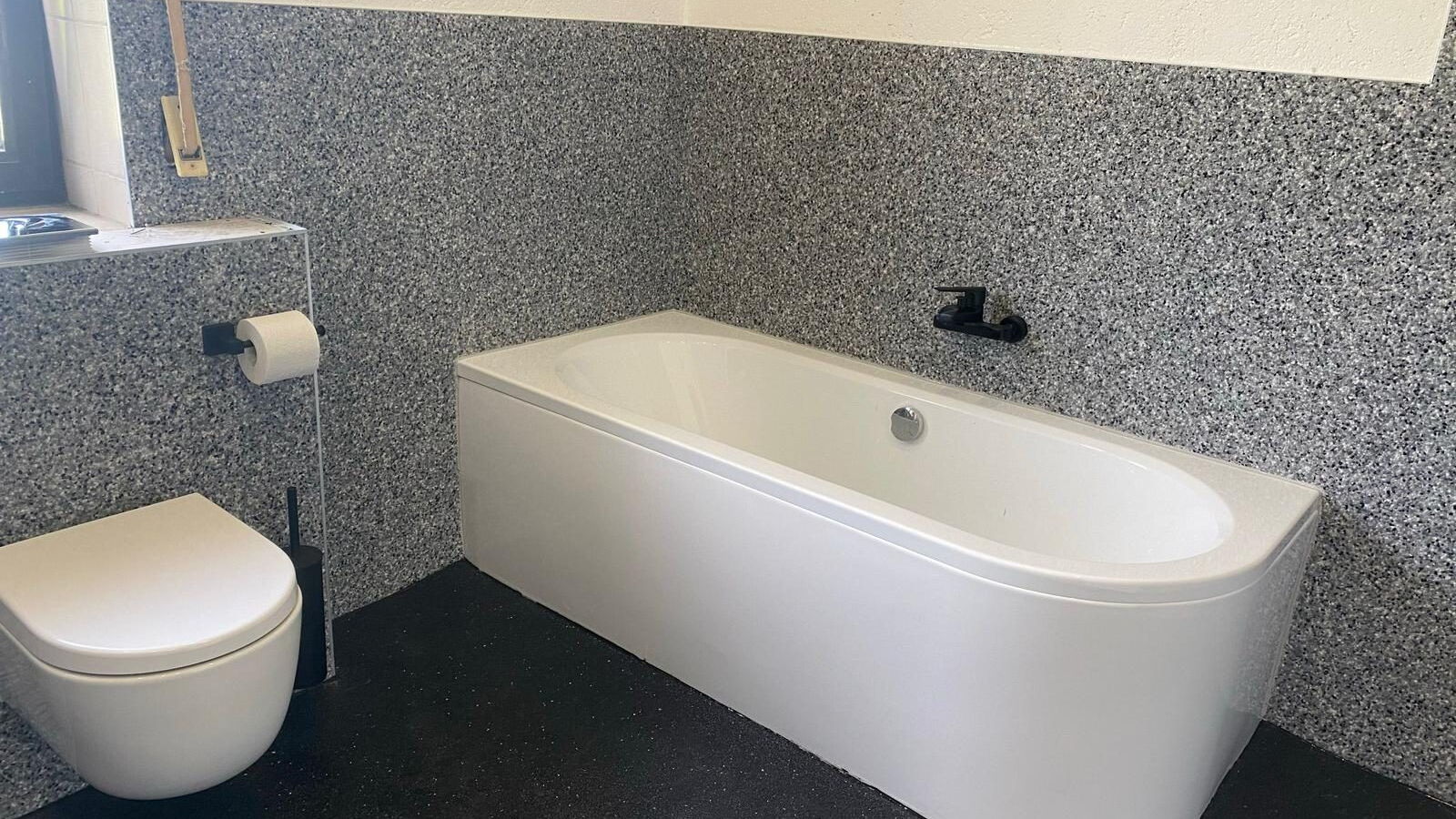 Badezimmer mit grauem Steinteppich an der Wand und schwarzem Boden, freistehende Badewanne
