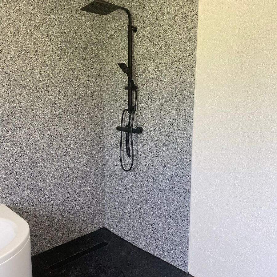 Bodengleiche Dusche mit grauem Steinteppich an den Wänden und schwarzem Boden mit Duschrinne