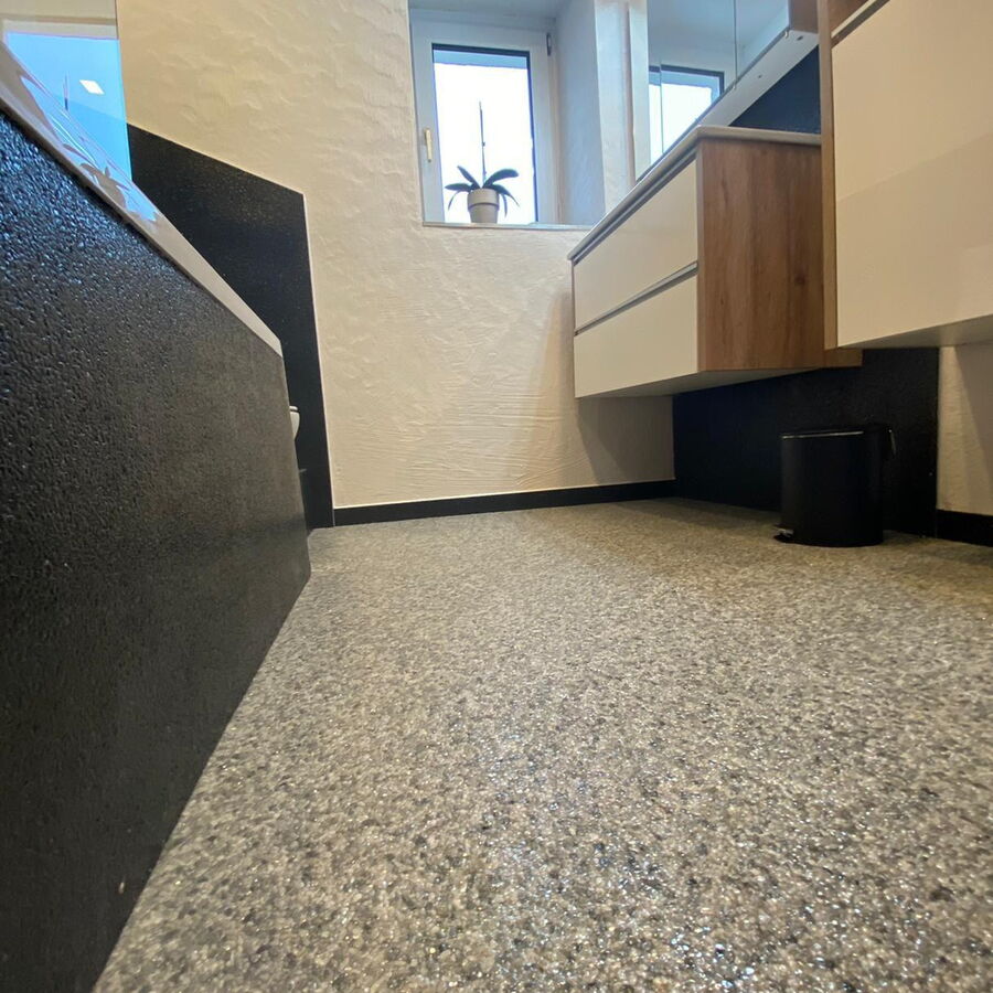 Gäste-WC mit hellgrauem Steinteppich als Bodenbelag und dunklem Sockel