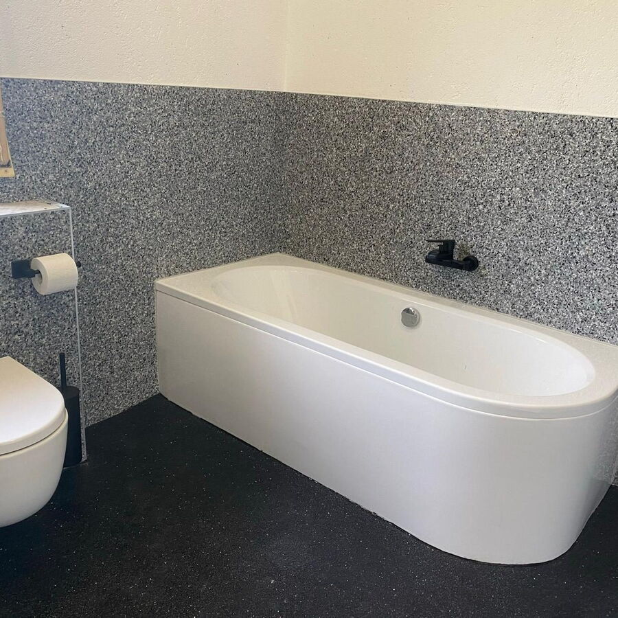 Badezimmer mit grauem Steinteppich an der Wand und schwarzem Boden, freistehende Badewanne